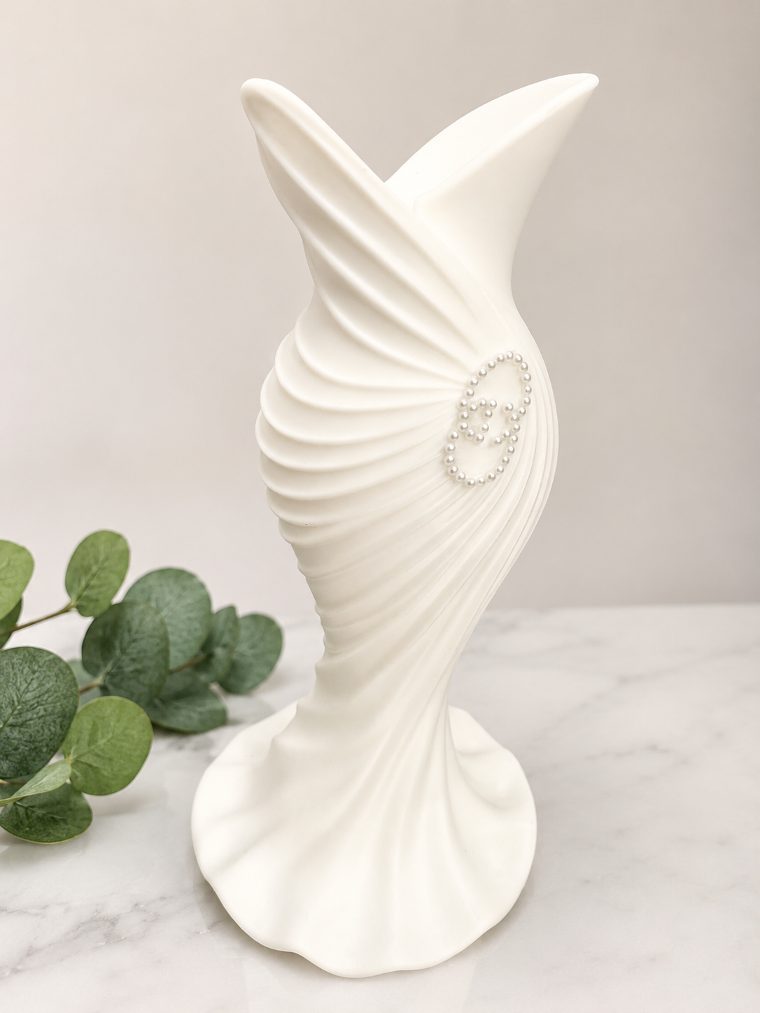 White spiral decorative vase with pearl accent on marble surface.