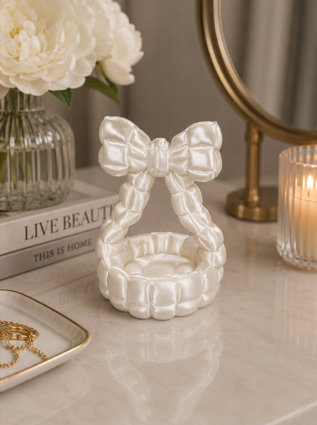 Luxury pearl white quilted bow trinket dish displayed on a vanity table with jewelry, flowers, and candle décor.